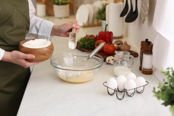 Woman adding flour into bowl at light table, closeup