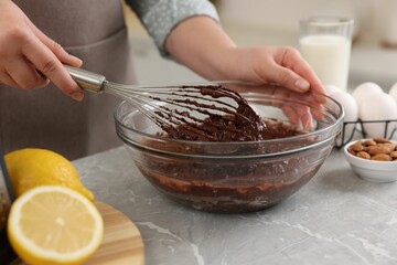 Woman mixing chocolate cream with whisk in bowl at gray marble table indoors, closeup
