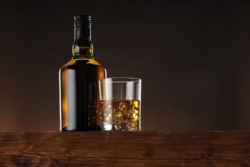Whiskey with ice cubes in glass and bottle on wooden table, low angle view. Space for text - obrazy, fototapety, plakaty