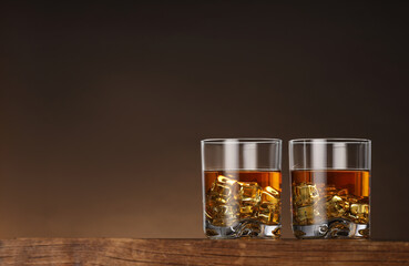 Whiskey with ice cubes in glasses on wooden table against brown background, space for text