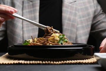 Stir-fry. Woman eating tasty noodles with meat and vegetables at dark table, closeup