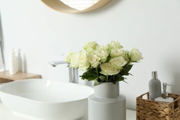 Vase with beautiful white roses and toiletries near sink in bathroom