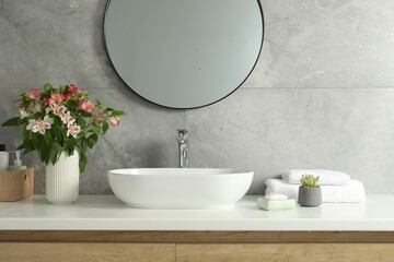 Vase with beautiful Alstroemeria flowers and toiletries near sink in bathroom