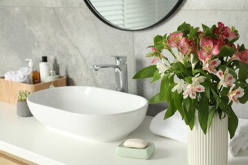 Vase with beautiful Alstroemeria flowers and toiletries near sink in bathroom