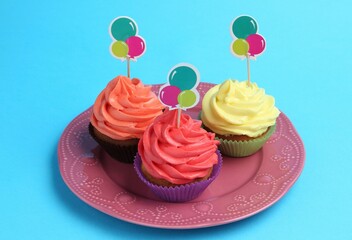 Delicious cupcakes with bright cream and toppers on light blue background