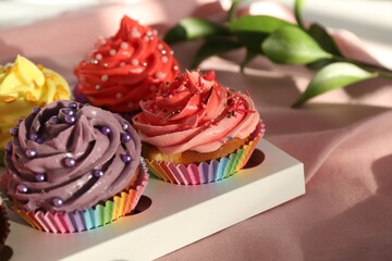 Delicious cupcake with bright cream on pink fabric, closeup