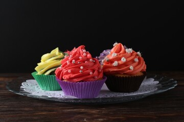 Delicious cupcake with bright cream on wooden table against black background