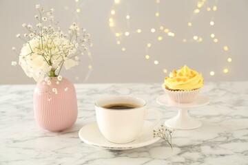 Delicious cupcake with yellow cream, coffee and flowers on white marble table