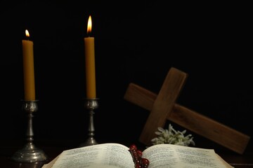 Church candles, Bible, cross and rosary beads on table against black background