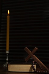 Church candle, Bible, cross and rosary beads on wooden table