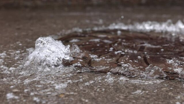 Water pipe burst, water Water flows out of the manhole onto the asphalt. The accident in the sewer. Leaking water supply system in the city on the road. Slow motion video