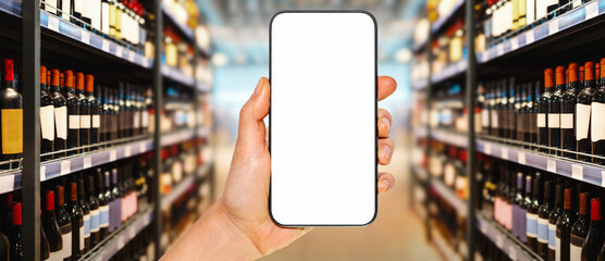 Mobile phone with blank screen mockup in female hand in front of liquor store.