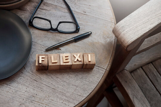 A view from above of wooden blocks arranged to spell the word "FLEXI" on a  wooden table. The blocks have a natural, rustic texture, with pen, eyeglasses at the side