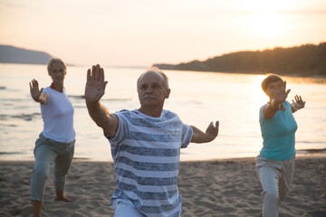 group elderly of people practice Tai Chi Chuan  at sunset on the beach.  Chinese management skill Qi's energy. Healthy lifestyle  - obrazy, fototapety, plakaty