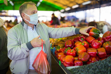 Man in face mask purchasing pepper in greengrocery