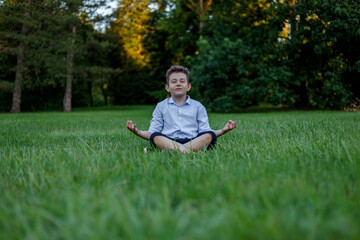 A teenager is meditating in the lotus position, doing yoga, in the park, sitting on the grass, with closed eyes.