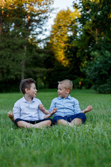 Naklejka na ściany i meble Two funny boys they sit in a yoga position, they look at each other and show their tongues, in the park.