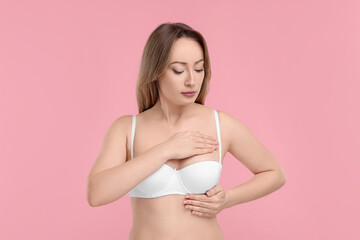 Fototapeta na wymiar Mammology. Young woman doing breast self-examination on pink background