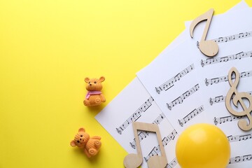 Baby songs. Music sheets, wooden notes, toy bears and ball on yellow background, top view with...