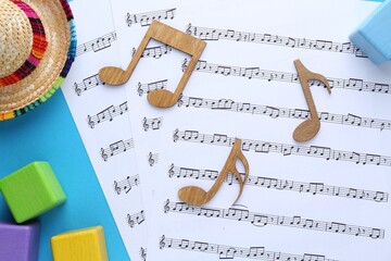 Baby songs. Music sheets, wooden notes, cubes and hat on light blue background, flat lay