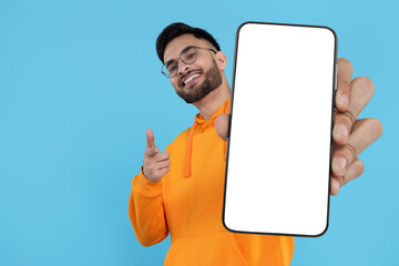 Happy man holding smartphone with empty screen on light blue background, space for text