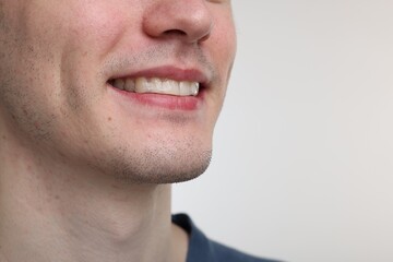Young man using whitening strip on light background, closeup. Space for text