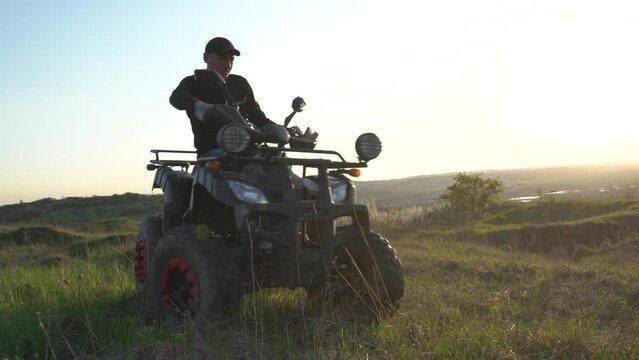 man riding quad bike at sunset, active recreation in nature, riding on a quad bike