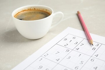 Sudoku, cup of coffee and pencil on light marble table, closeup