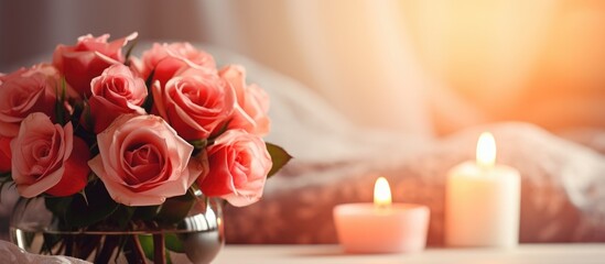 A vase filled with pink roses sits next to a flickering lit candle on a table indoors. The soft glow of the candle illuminates the delicate petals of the roses, creating a warm and inviting ambiance.