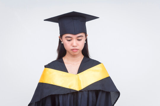 Young female graduate in cap and gown appears sad and disappointed, possibly due to the absence of family or significant other.