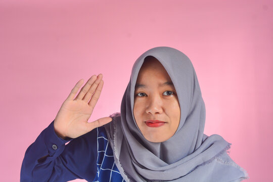 Copy space. A young Indonesian woman in blue clothes and gray hijab posing in front, looking to the left and pointing something in the same direction and full of confidence