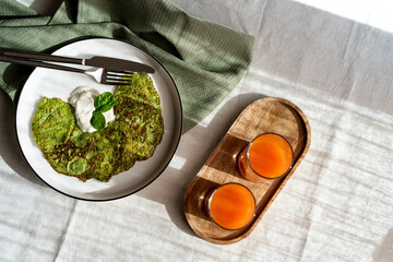 Spinach pancakes with sour cream on a plate and carrot juice in glasses. Healthy breakfast