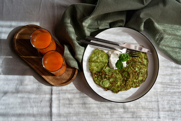Top view of healthy meal. Spinach pancakes with sour cream on a plate and carrot juice in glasses. Delicious healthy breakfast