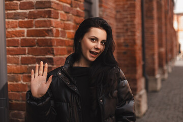 Happy attractive woman in black bomber, walk outdoors, meeting her friends or love, showing high...
