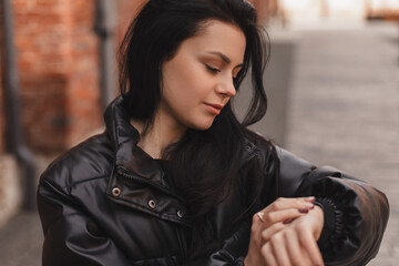 Checking time. Smiling teen girl standing near brick wall background looking at her watch while...