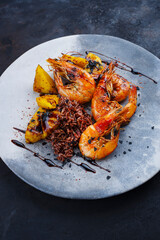 Traditional fried king prawns with pineapple pieces and brown rice served as close-up on a design bowl with text space