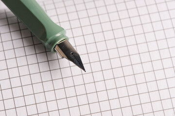 Green fountain pen lies on white sheets checkered notebook.