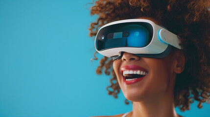 Close-up of young laughing enthusiastic woman wearing white augmented virtual reality glasses on studio blue background with copy space