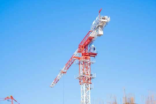 Red and white luffing jib tower crane standing tall against a clear bright blue sky on a construction site.