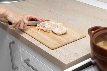woman cutting chicken breast on kitchen board.