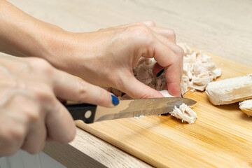 woman cutting chicken breast on kitchen board.