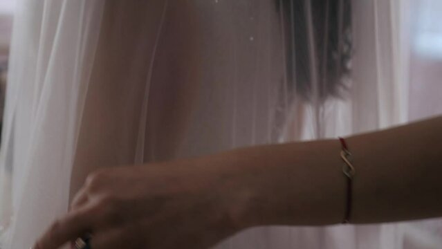 A bridesmaid or cutter helps a bride tie the intricate lacing of her shimmering wedding dress