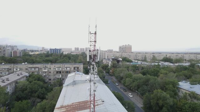Aerial footage around a telecommunications tower with sector antennas of a mobile operator and radio relay equipment in the city. Telecommunication equipment in Kazakhstan. 5G technology. Telecomphone