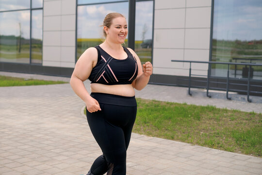 A fat, obese, happy, smiling woman in sports clothes on a jog. A person is running down a city street