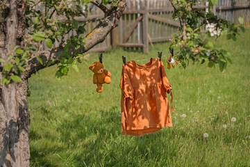 A girl's dress and washed soft plush toys are drying on a clothesline in the garden under a tree