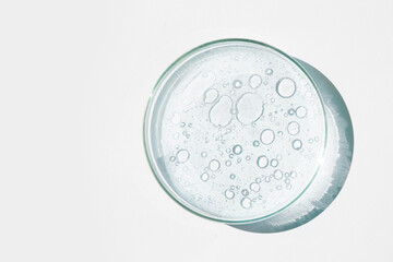 Petri dish. Petri's cup with liquid. Chemical elements, oil, cosmetics. Gel, water, molecules, viruses. Close-up. On a white background.