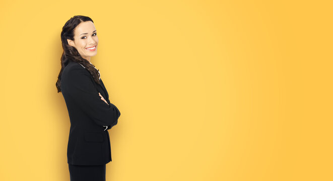 Happy smiling attractive businesswoman, with blank space area for ad slogan or advertising text. Confident brunette woman wear black suit isolated yellow studio wall background. Business ad concept.