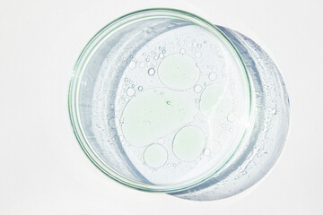 Petri dish. Petri's cup with liquid. Chemical elements, oil, cosmetics. Gel, water, molecules, viruses. Close-up. On a white background.