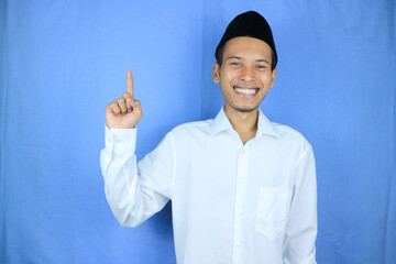 Smiling expression of muslim asian man, pointing finger an empty space. Advertising concept