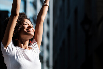 Cheerful woman model with arms up in the street.